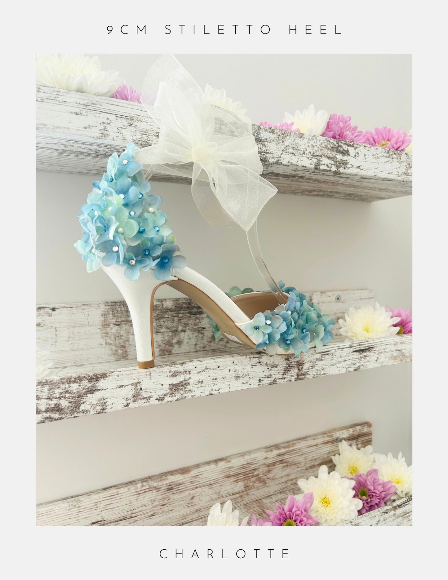 Ivory High-heeled bridal shoe with floral design on a wooden shelf with flowers.