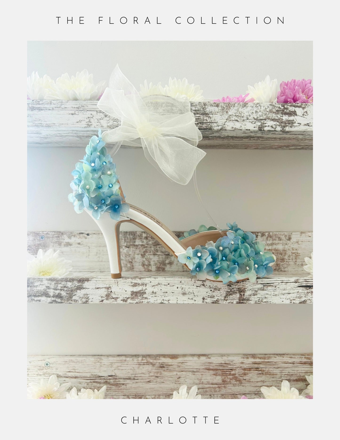 Ivory peep toe high-heeled shoes with blue floral decorations on a wooden surface, labelled 'The Floral Collection'.