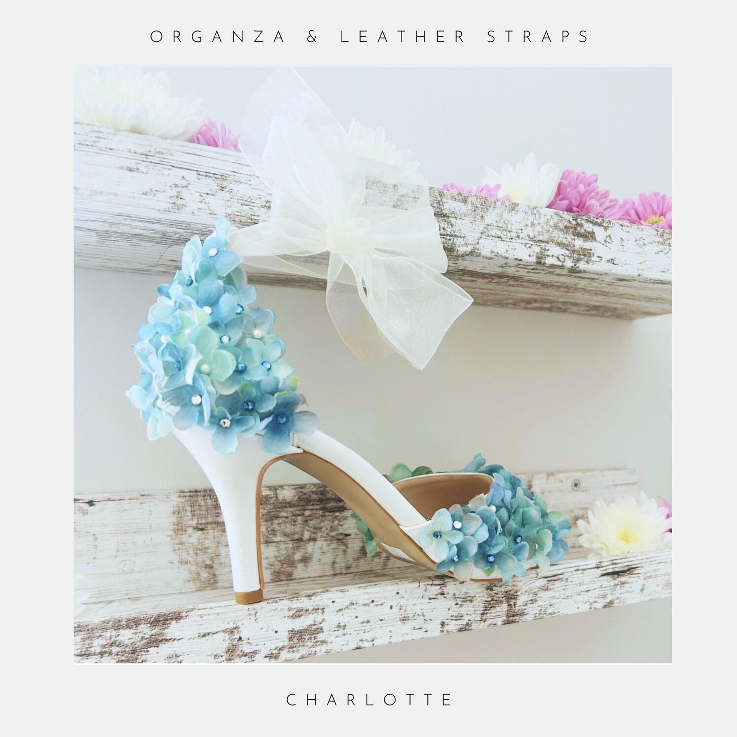 Ivory High-heeled bridal shoe with floral design on a wooden shelf with flowers.