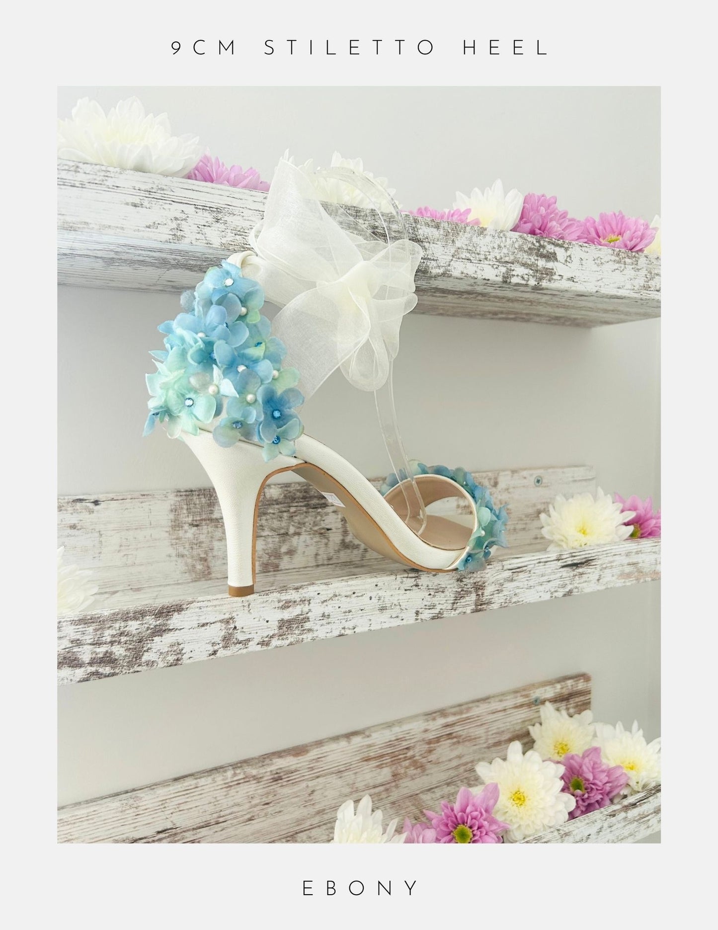 Ivory high-heeled wedding shoe with floral design on a wooden shelf with flowers.