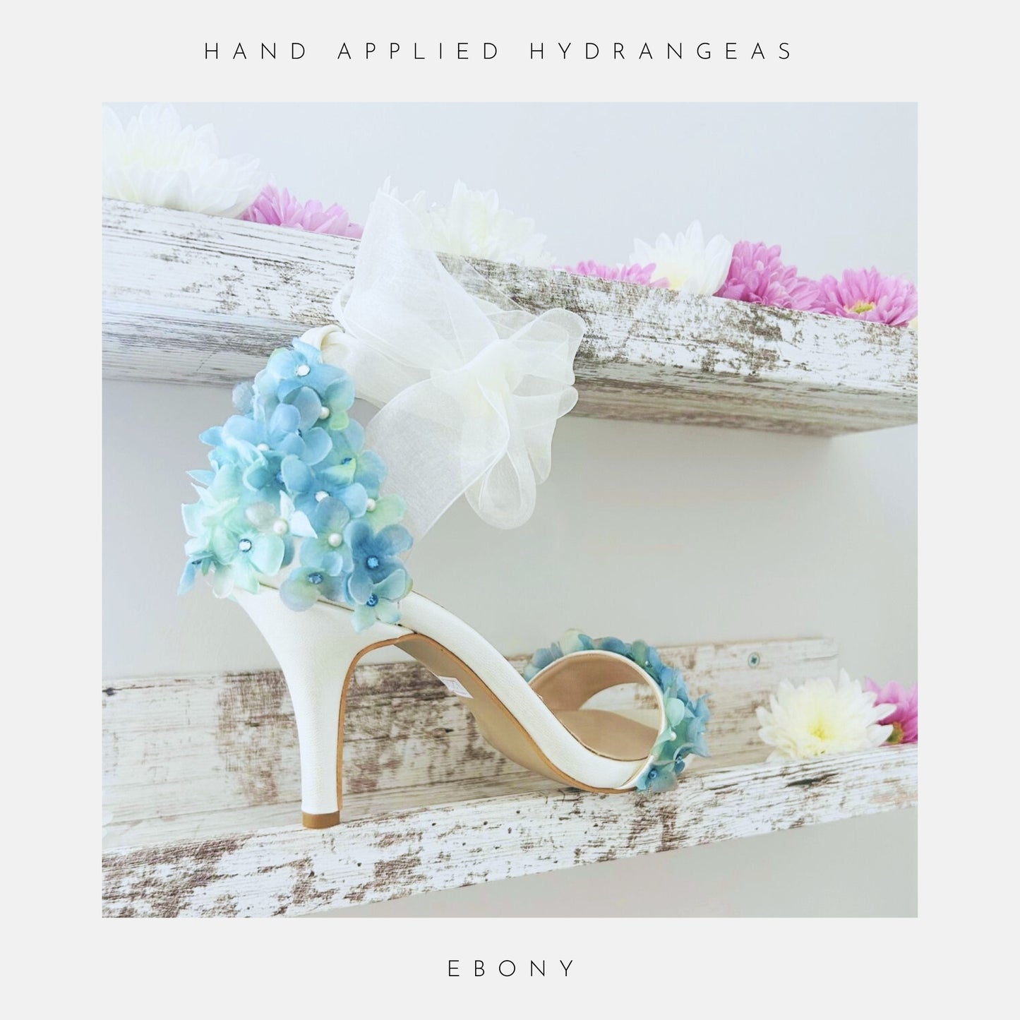 Ivory high-heeled wedding shoe with floral design on a wooden shelf with flowers.