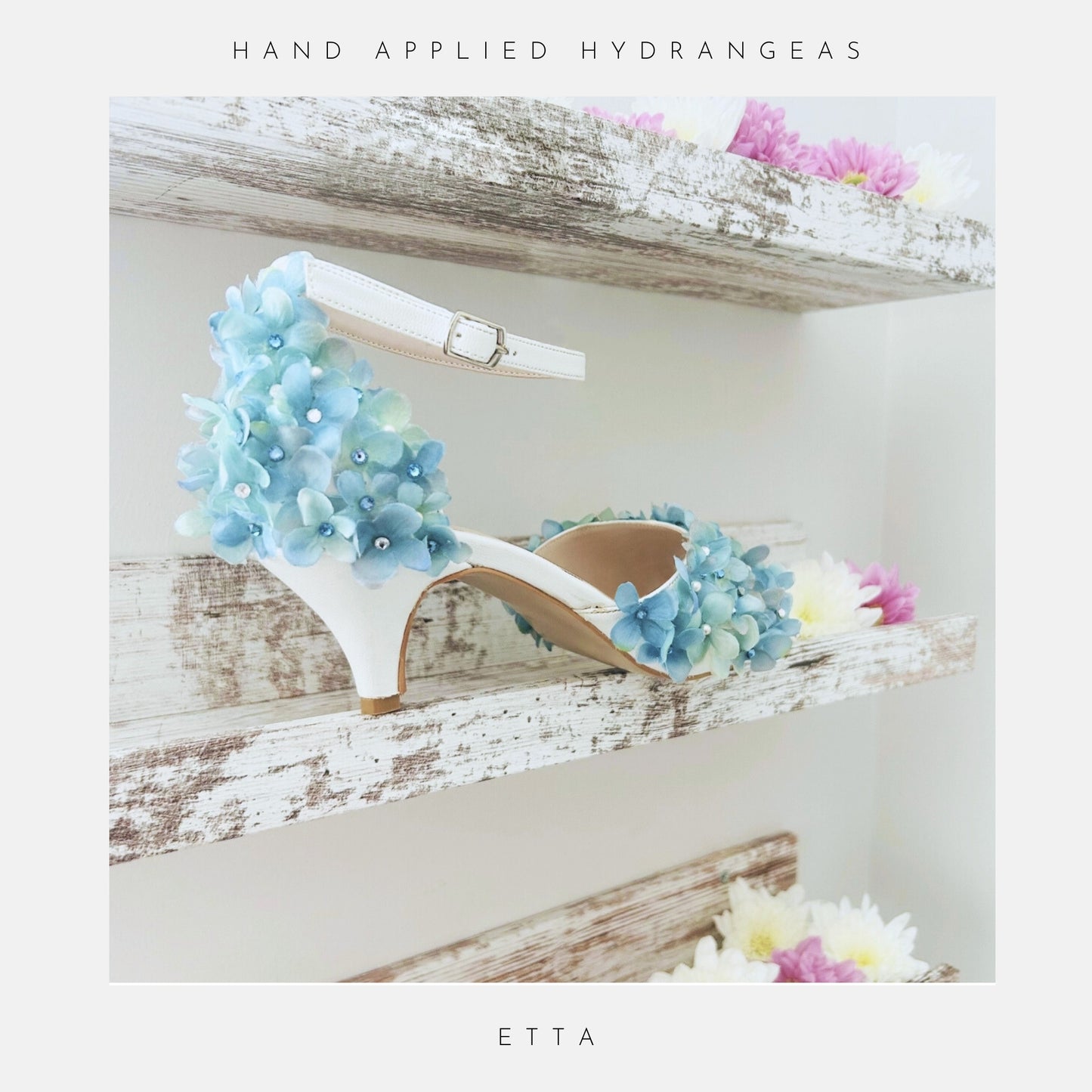 Ivory peep toe high-heeled shoe with floral design on a wooden shelf with flowers.