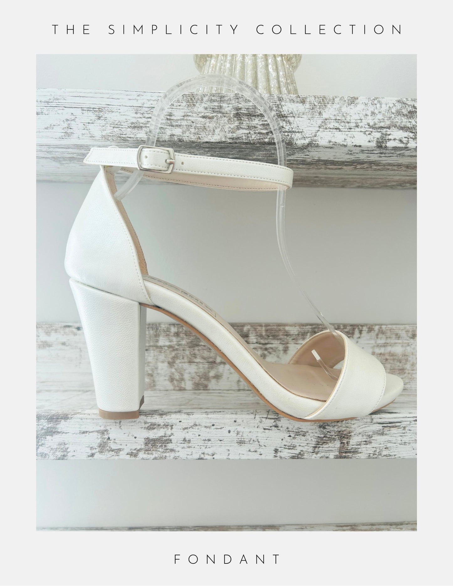 A white high-heeled sandal with an ankle strap from Phoenix England—Callie Organza Strap High Block Bridal Shoes—rests on a rustic wooden shelf. The Simplicity Collection appears above and Fondant is written below. Perfect for a chic bridal look.
