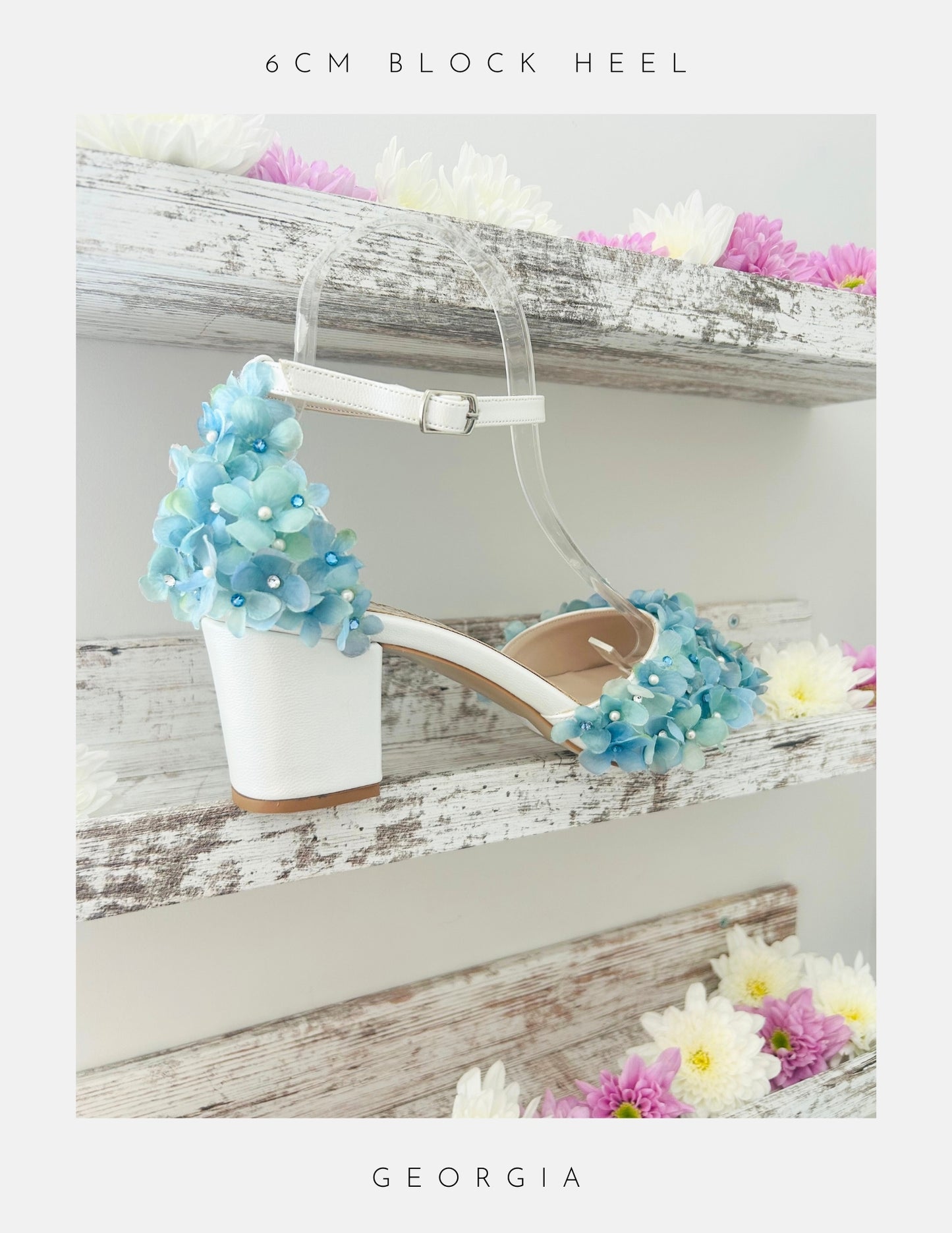 Ivory low block heel wedding sandal with blue floral decorations on a wooden surface with flowers.