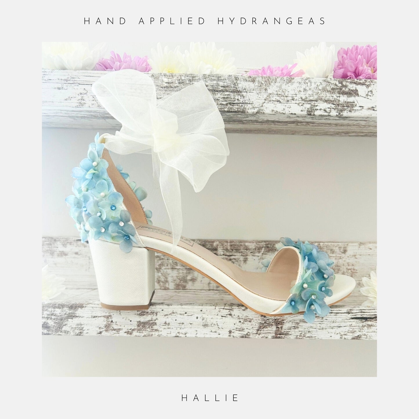 Ivory bridal sandal with floral decorations on a wooden surface with flowers in the background, labelled 'Hand Applied Hydrangeas' and 'Hallie'.
