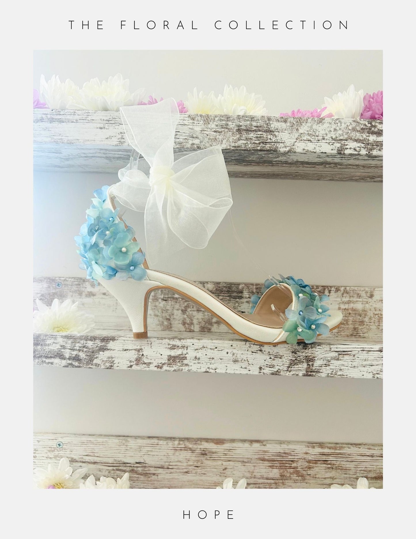 The Hope Organza Floral Kitten Heel Bridal Shoes by Phoenix England—a white sandal with blue and white flowers and a sheer bow rests on a rustic shelf among pastel blooms. Text: The Floral Collection and Hope. Perfect for brides.