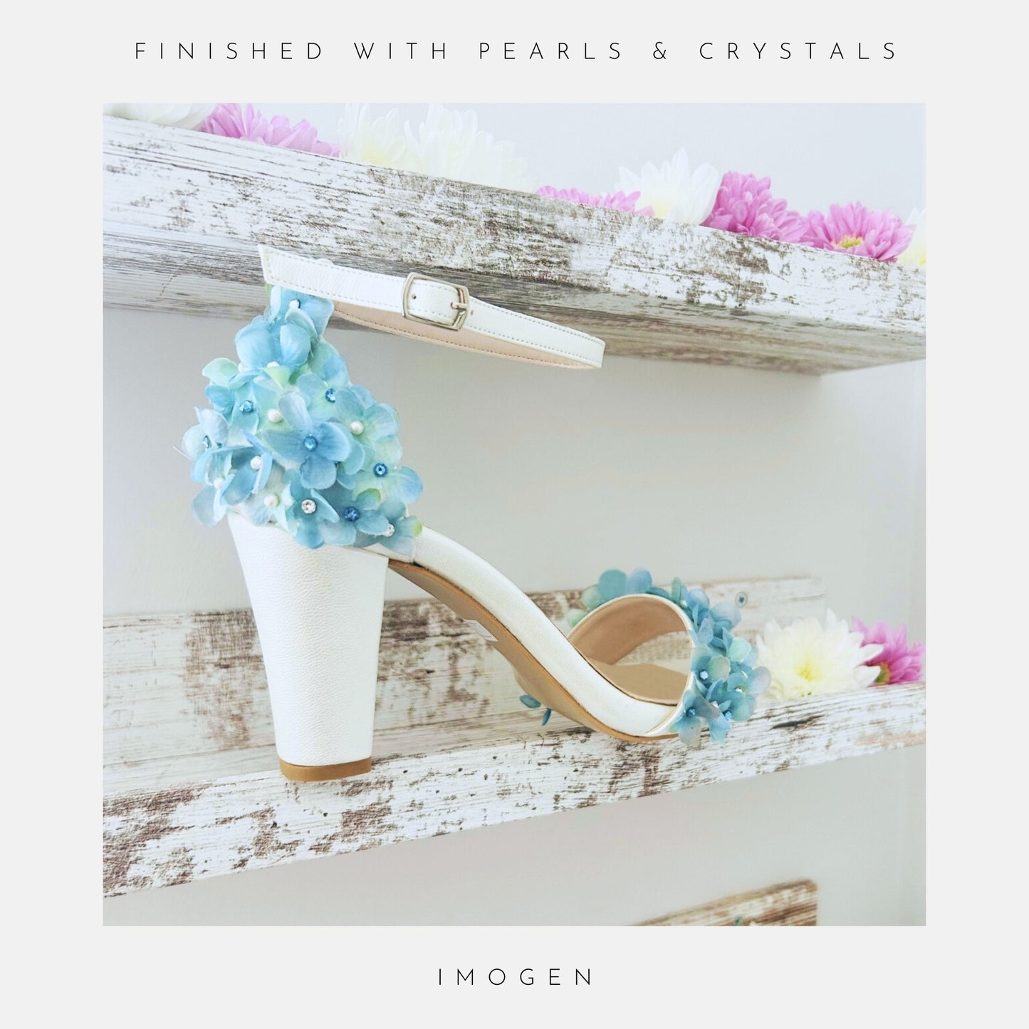 Ivory high-heeled block heel bridal shoe with blue floral decorations on a wooden shelf with flowers.