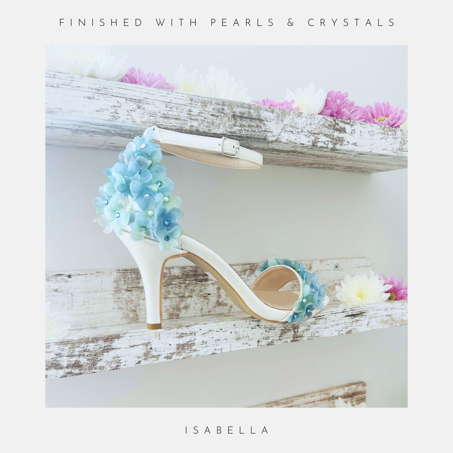 Ivory high-heeled bridal shoe with floral decorations on a wooden shelf with flowers.