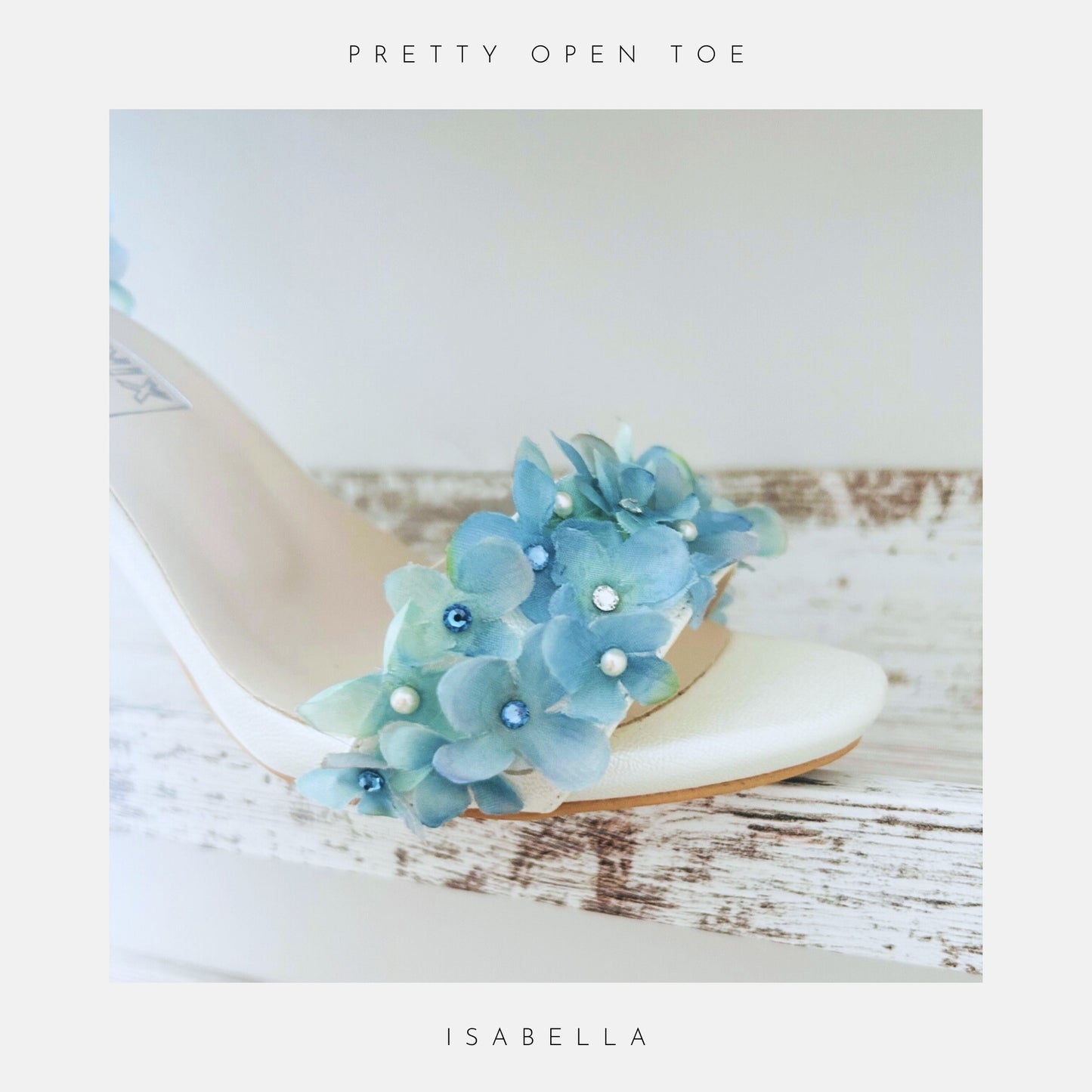 Ivory sandal with blue floral embellishments on a wooden surface, featuring 'Austrian Crystals & Pearls' text.