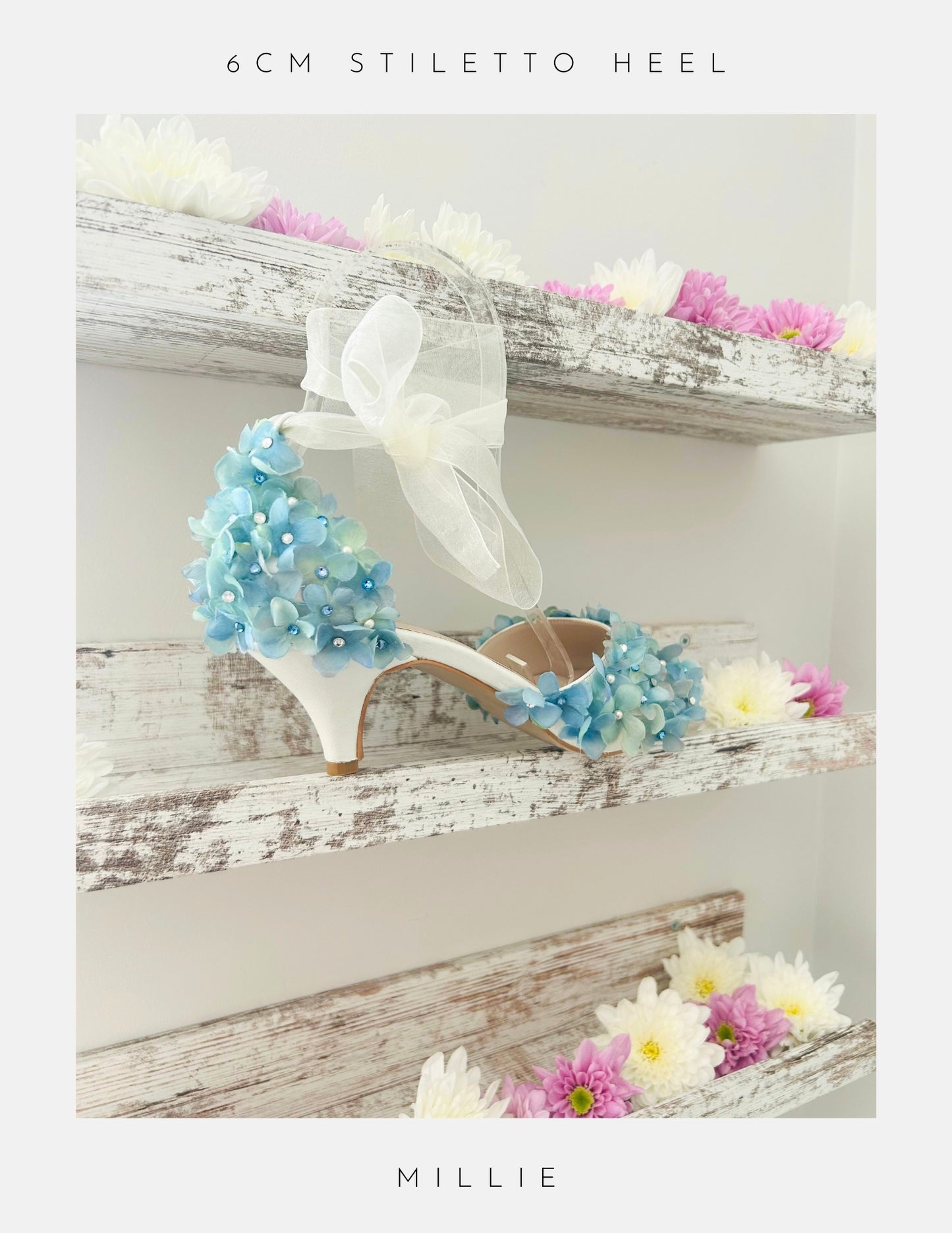 Ivory high-heeled shoes with blue floral embellishments on a wooden surface with flowers.