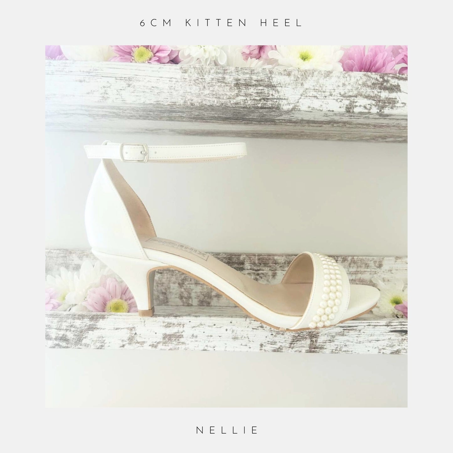 An ivory Nellie Pearl Kitten Heel Bridal Shoe by Phoenix England with an ankle strap and pearl embellishments sits on rustic wooden shelves adorned with pink and white daisies. Text above: 6cm kitten heel; below: Nellie.