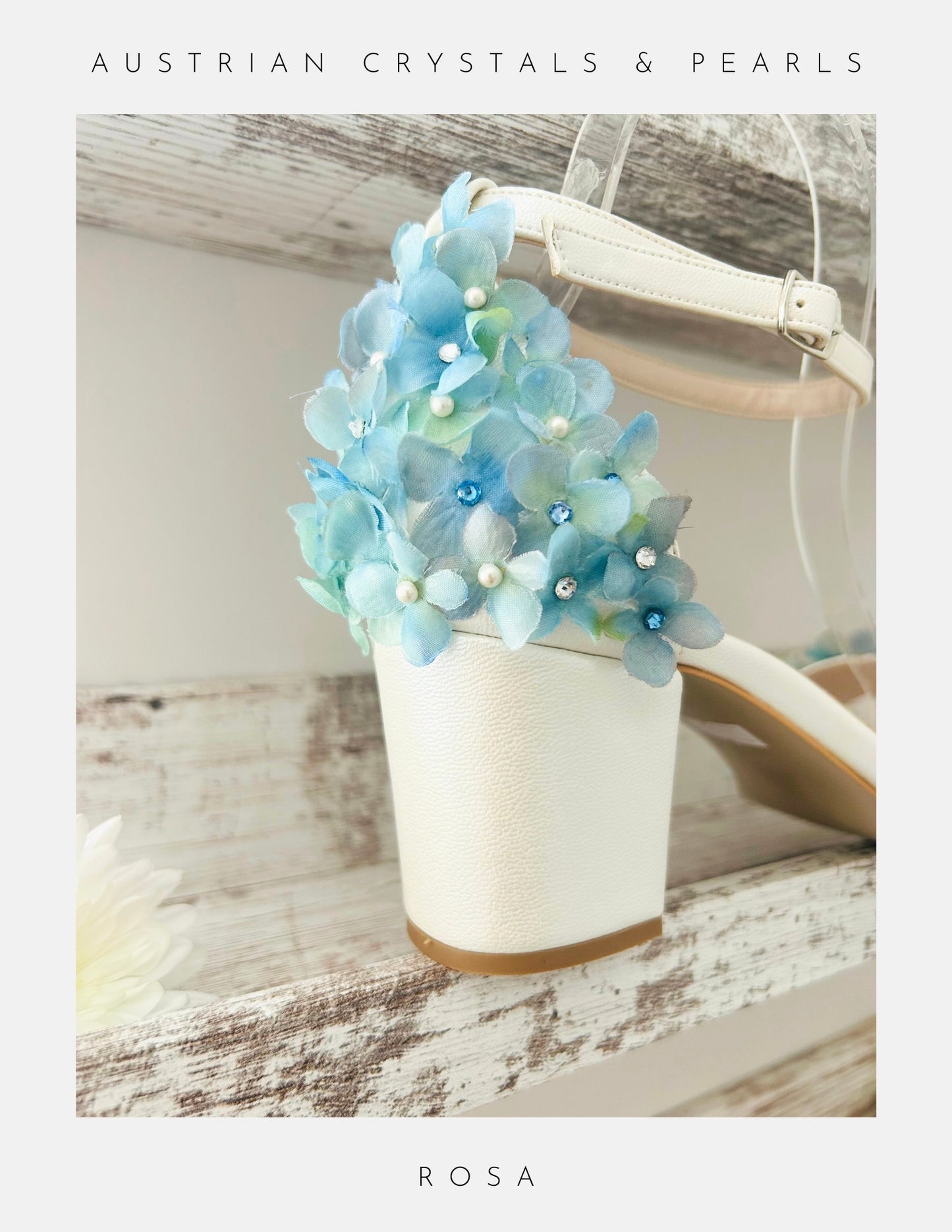 The Rosa Floral Low Block Heel Bridal Shoes by Phoenix England feature a white design with ankle strap, blue and light green floral details, Austrian crystals, and pearl embellishments on the heel. Text: Austrian Crystals & Pearls and ROSA.