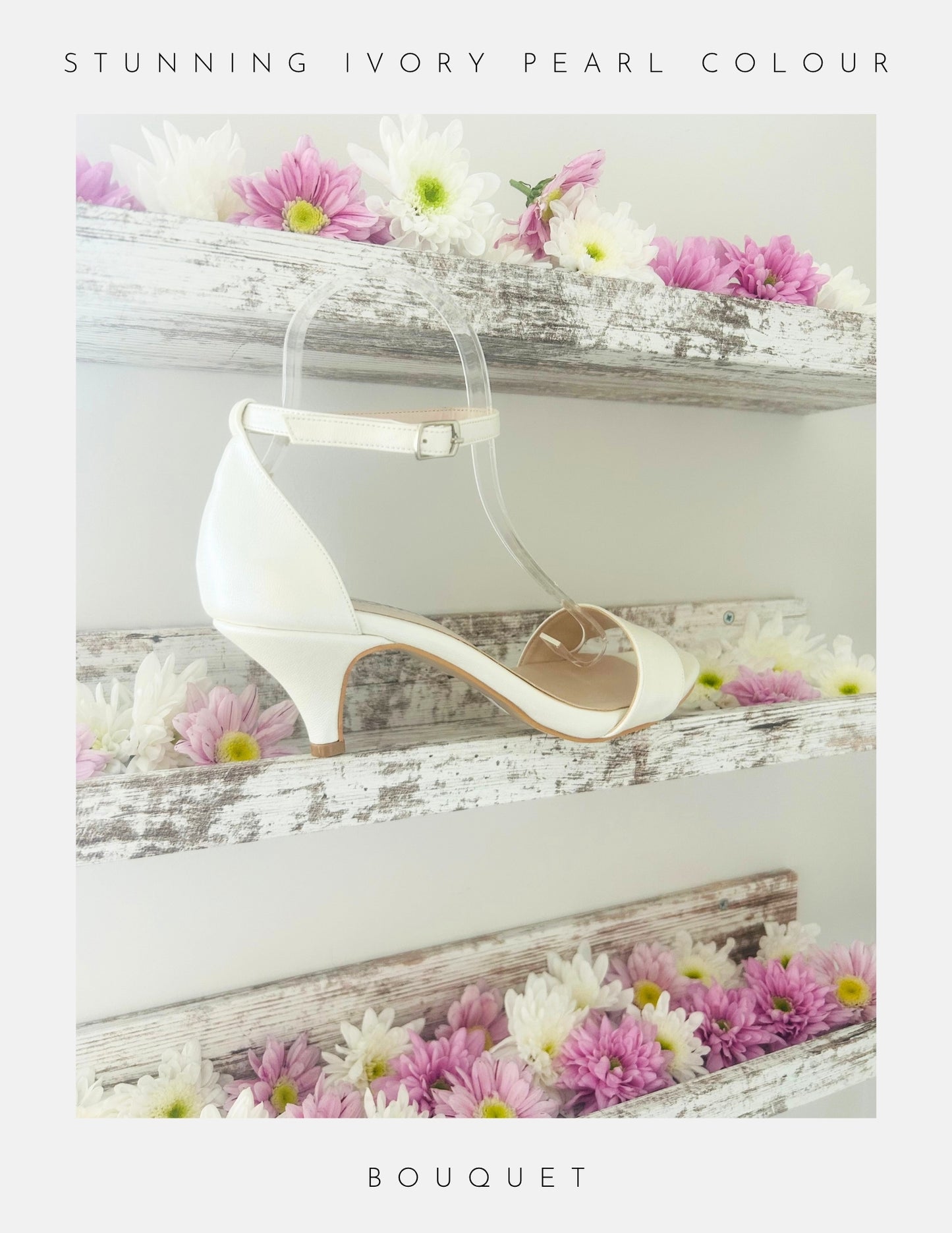 The Bouquet Kitten Heel Bridal Shoes by Phoenix England feature an ivory pearl vegan leather finish and ankle strap, displayed on a rustic white shelf among pink, white, and lavender daisies. Text reads Stunning Ivory Pearl Colour and Bouquet.
