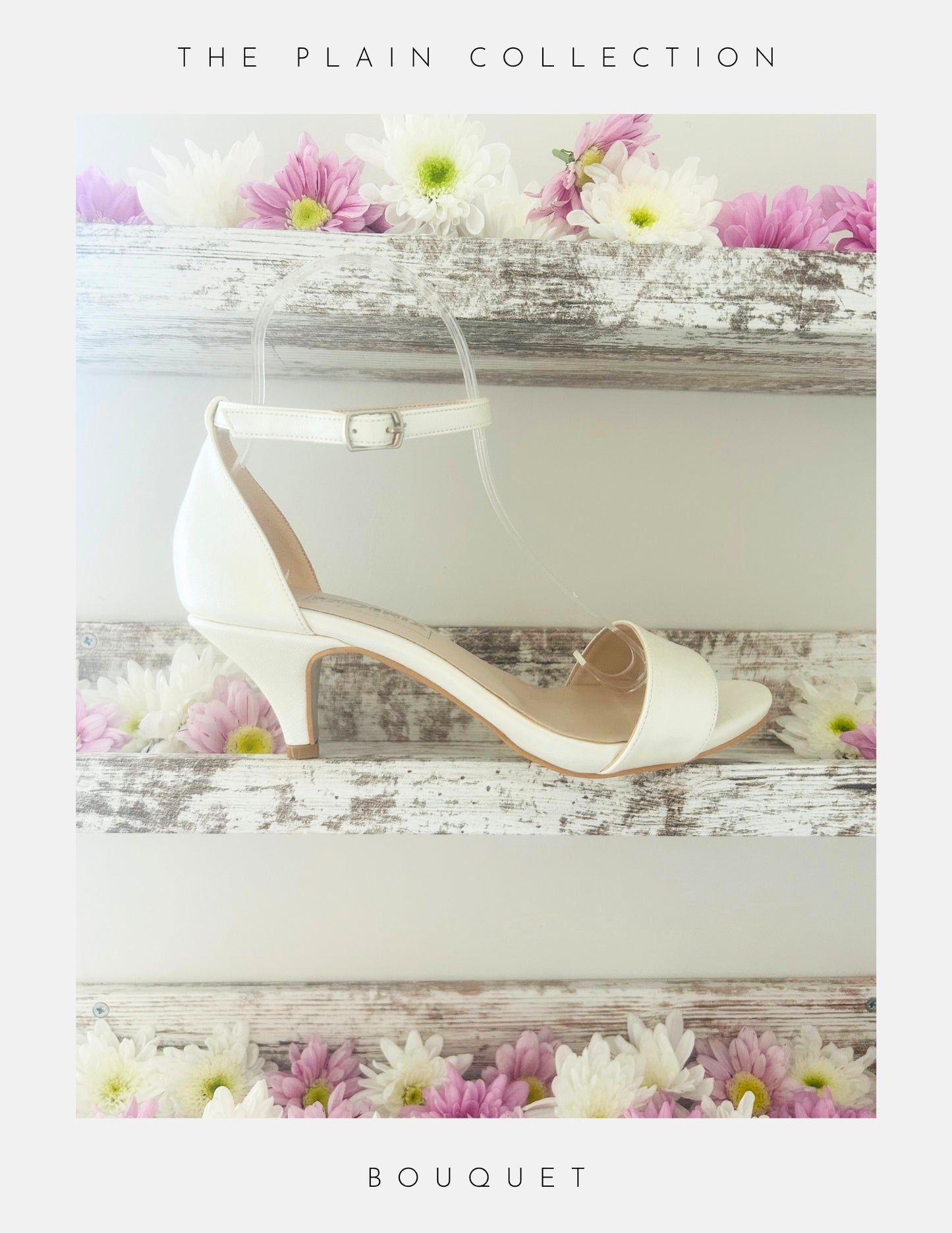 A pair of Bouquet Kitten Heel Bridal Shoes by Phoenix England in pearl vegan leather with an ankle strap rests on a rustic white shelf, surrounded by pink and white daisies. The Plain Collection—perfect bridal heels for your special day.