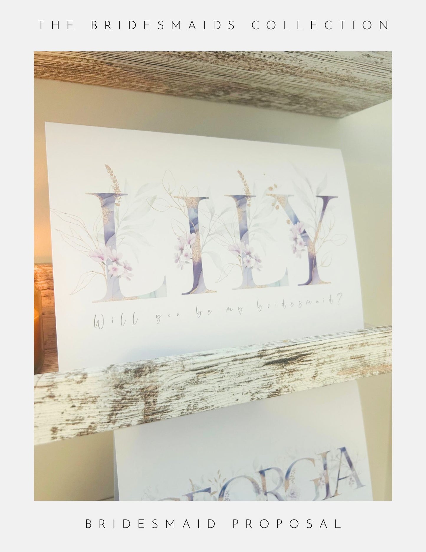 A Phoenix England Bridesmaids Proposal Sterling Silver card with soft florals and “Will you be my bridesmaid?” for Lily sits on a rustic wooden shelf, while another card peeks below with partial name and bordered text.