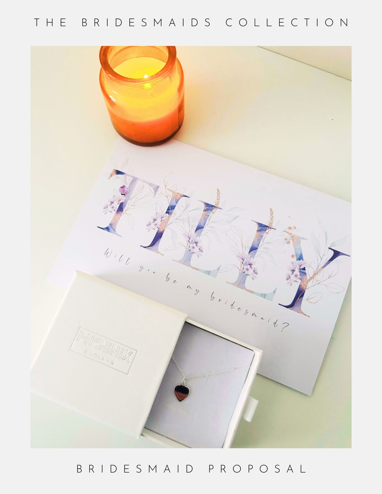 A white box with the Phoenix England Bridesmaids Proposal Sterling Silver heart necklace, a floral Will you be my bridesmaid? card, and a lit orange candle are arranged on a light surface. Text above: THE BRIDESMAIDS COLLECTION.
