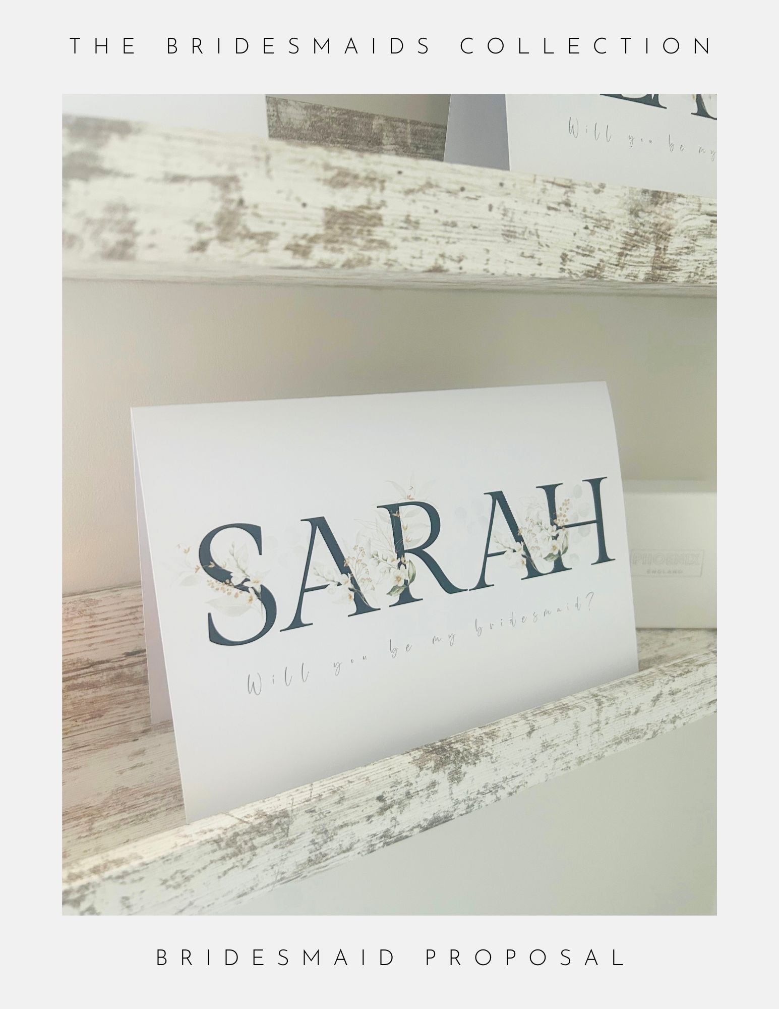 A card on a rustic white shelf reads SARAH with floral accents and Will you be my bridesmaid? beneath it. The image features Bridesmaids Proposal Cards by Phoenix England, with sterling silver jewellery to make the moment extra special.