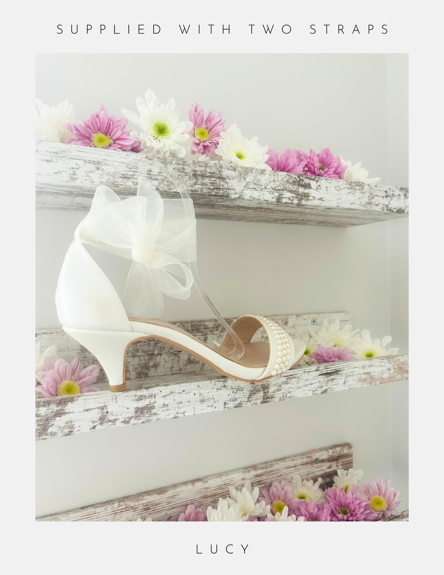 Ivory high-heeled bridal shoe with a bow and open toe with pearls, placed on a wooden surface with flowers.