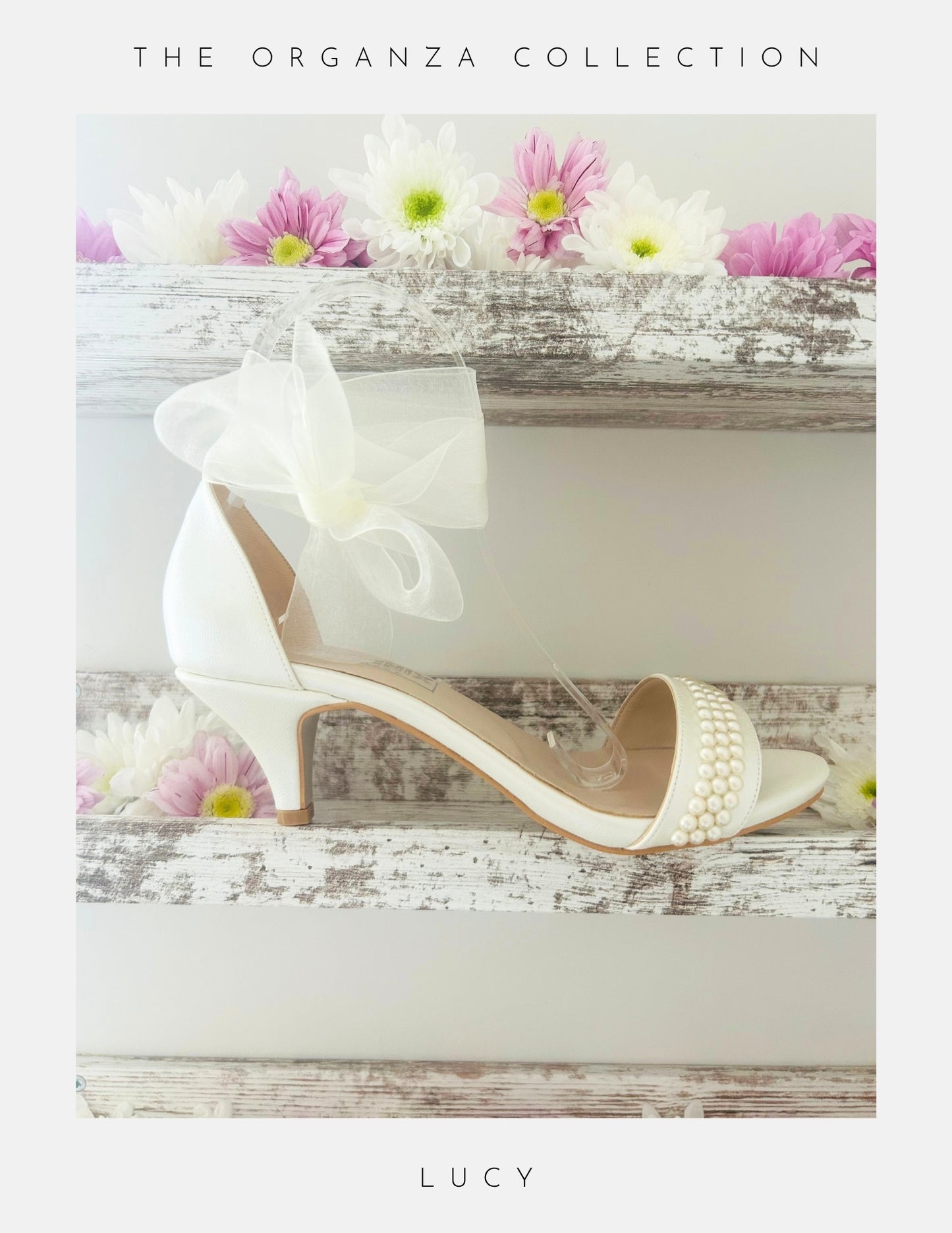 Ivory open toe pearl bridal sandal with pearls on a wooden surface with flowers, labelled 'The Organza Collection' and 'Lucy'.