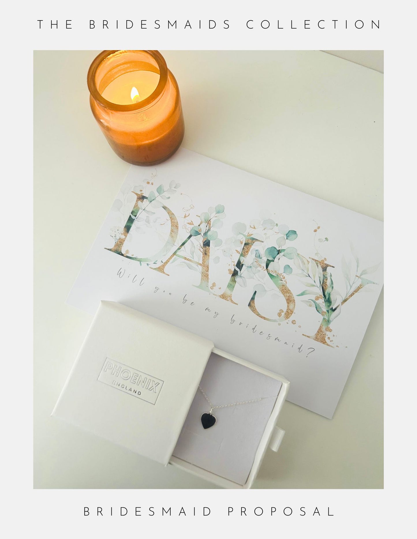 Surprise your Maid of Honour with a Phoenix England proposal set: a lit amber candle, floral card, and an open white box holding delicate sterling silver jewellery from our Maid Of Honour Collection featuring a black heart pendant.