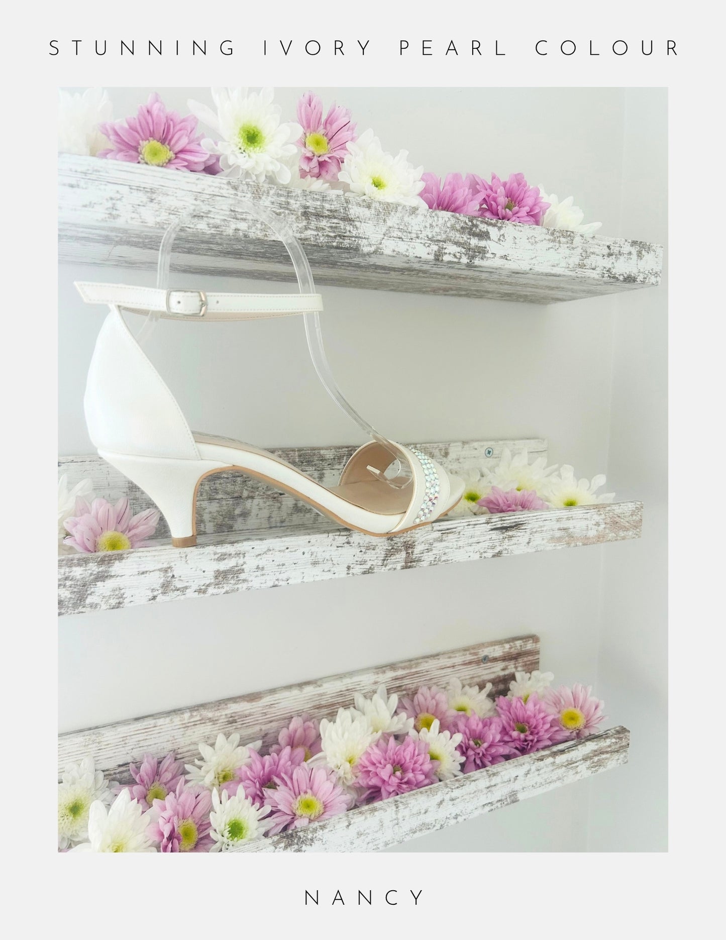 A pair of Nancy Crystal Kitten Heel Bridal Shoes by Phoenix England, in pearl vegan leather with ankle strap, is displayed on rustic white shelves adorned with daisies. Text above reads STUNNING IVORY PEARL COLOUR and below, NANCY.