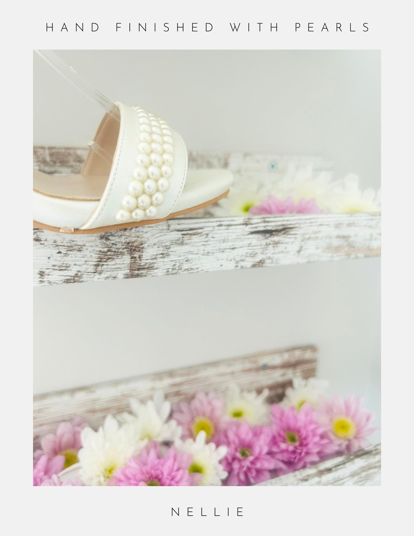 The Nellie Pearl Kitten Heel Bridal Shoes by Phoenix England are displayed on a rustic white wooden shelf above pastel flowers. Text reads Hand finished with pearls at the top and Nellie at the bottom.