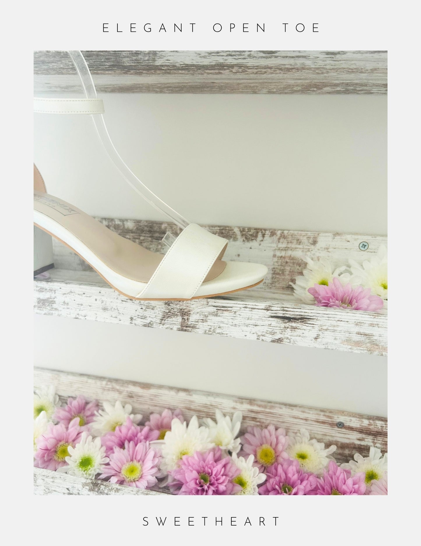 Close up of front of open toe wedding sandal in ivory on a wooden surface with flowers