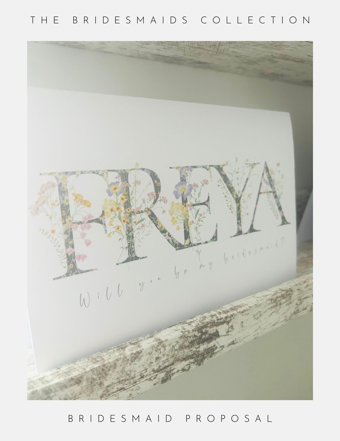 A card from Phoenix England’s Thank You Bridesmaid Gift Ideas, with floral “FREYA” letters and “Will you be my bridesmaid?”, sits on a rustic shelf, perfect for your special bridesmaid proposal or paired with bridesmaid jewellery.
