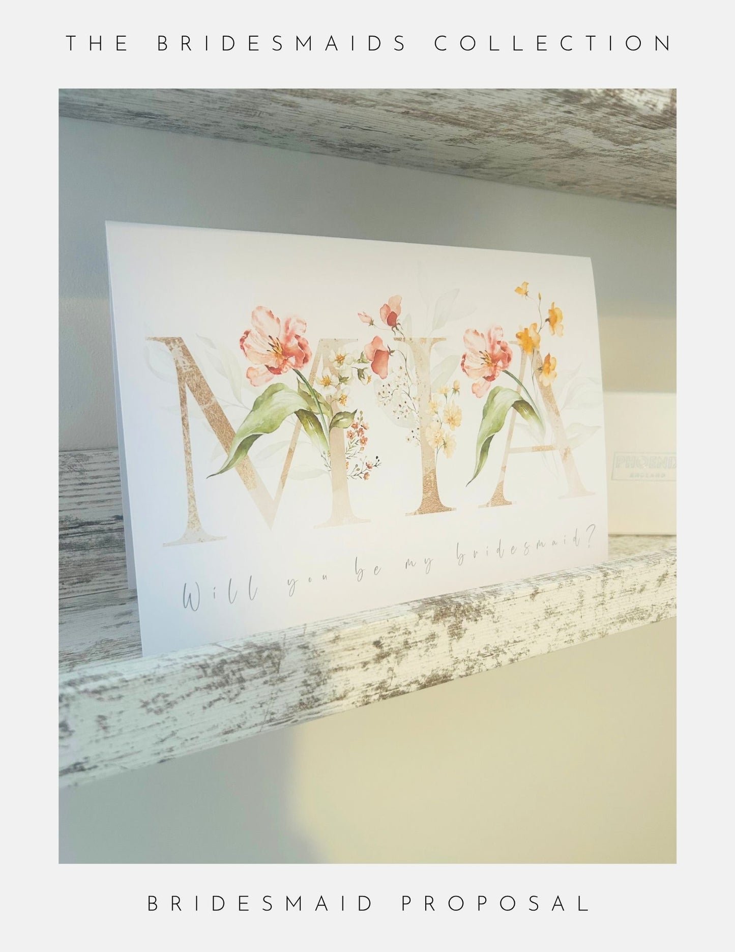 A Phoenix England Will You Be My Bridesmaid Gifts card with delicate flowers and MIA in elegant script sits on a rustic wooden shelf, perfect for pairing with bridesmaid gifts like sterling silver jewellery.