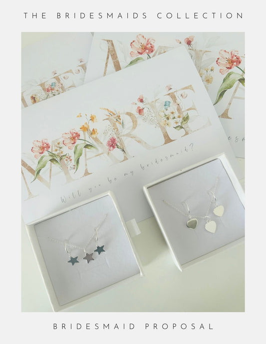 Two jewelry boxes with sterling silver jewellery—one with three star pendants, the other with two heart pendants—plus floral “Will You Be My Bridesmaid?” cards by Phoenix England make perfect bridesmaid gifts from the Will You Be My Bridesmaid Gifts collection.
