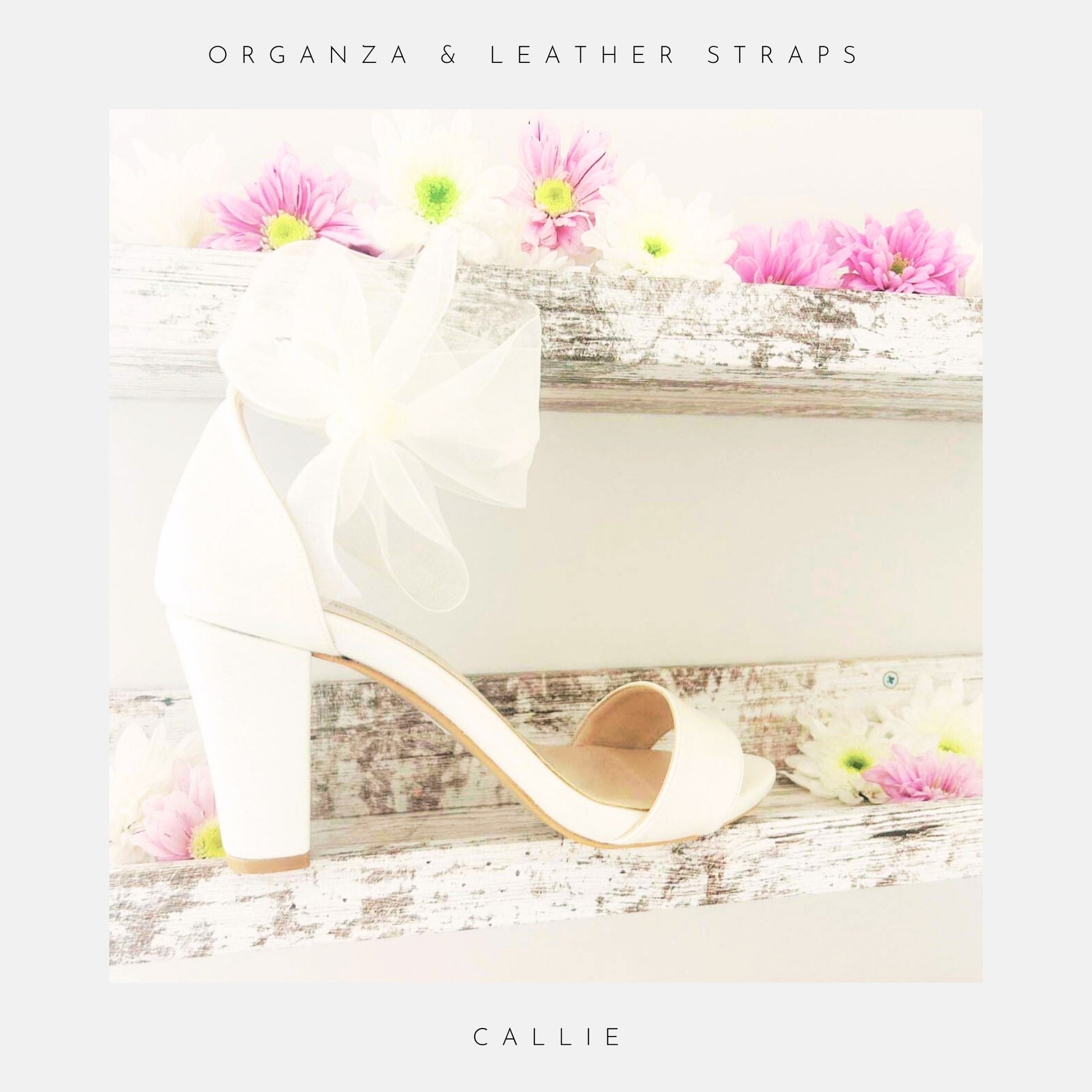 Ivory high-heeled shoe with an organza bow, placed on a wooden surface with flowers.