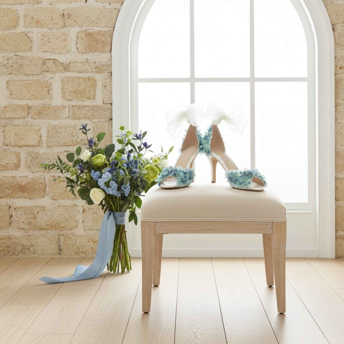 Bouquet of flowers and high-heeled shoes with floral decorations on a chair against a brick wall.