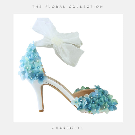 Blue floral high-heeled bridal shoe with blue flowers and organza strap on a white background, labelled 'The Floral Collection' and 'Charlotte'.