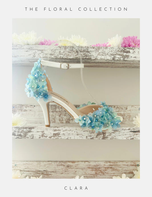 Ivory high-heeled peep toe wedding shoe with blue floral embellishments on a wooden surface.