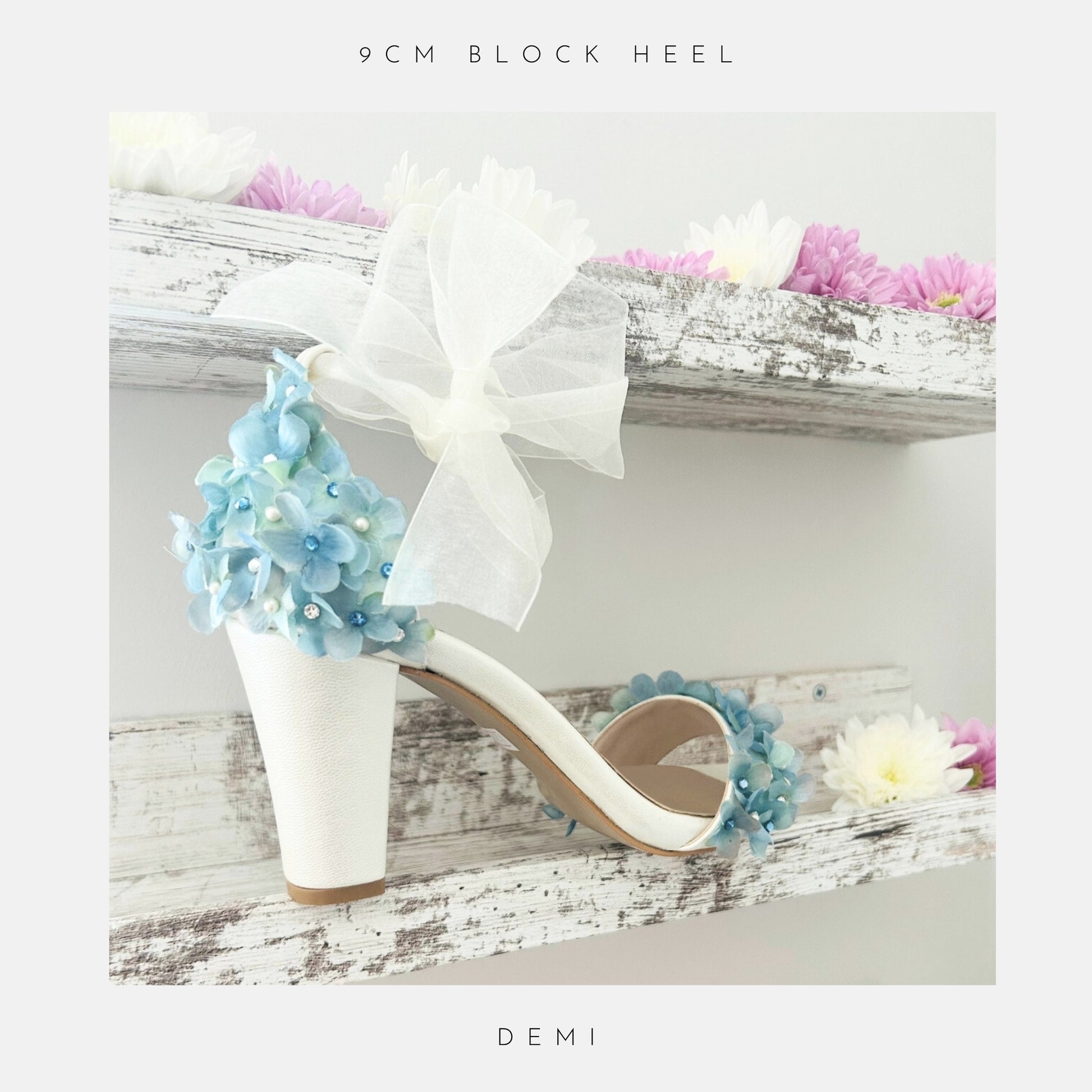 Ivory high-heeled shoes with floral decorations on a wooden shelf with flowers.