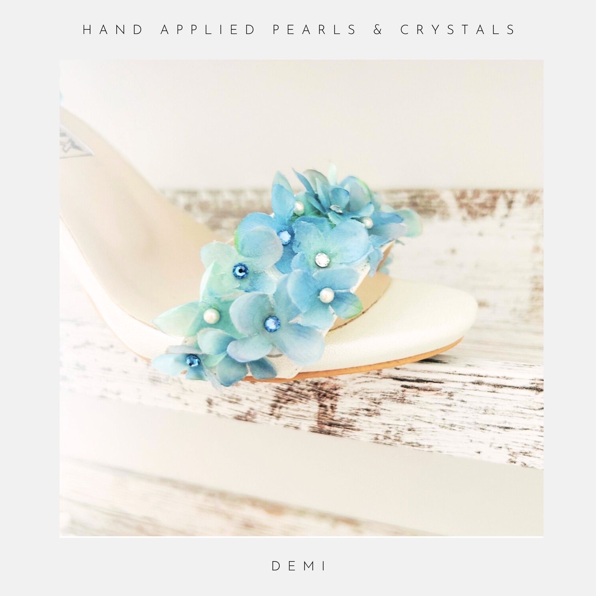 Ivory bridal sandal with blue floral embellishments on a wooden surface, labelled 'Austrian Crystals & Pearls' and 'Demi'.