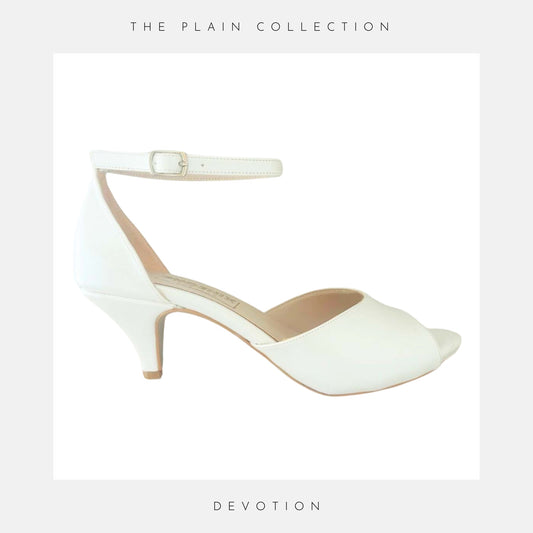 Ivory high-heeled shoe with ankle strap on a light grey background, labelled 'The Plain Collection' and 'Devotion'.