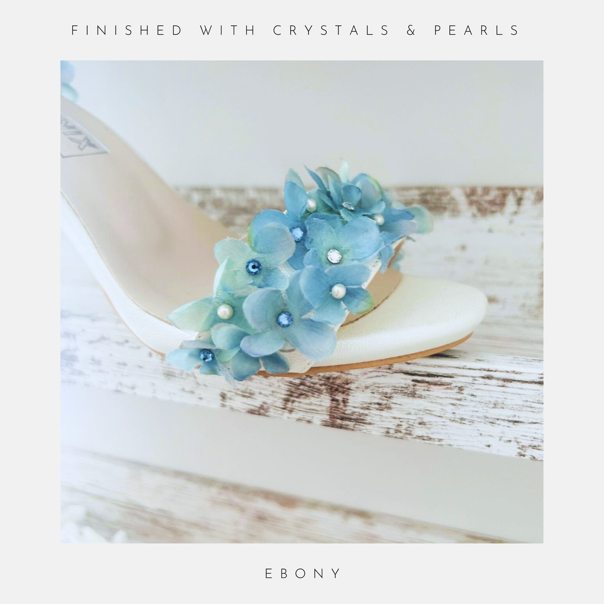 Ivory sandal with blue floral embellishments on a wooden surface, labelled 'Finished With Crystals & Pearls' and 'Ebony'.