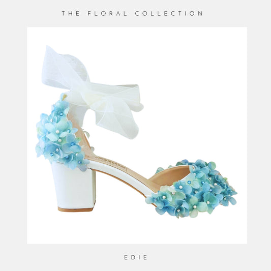 Ivory low block heeled shoes with blue floral embellishments on a white background, labelled 'The Floral Collection' and 'Edie'.