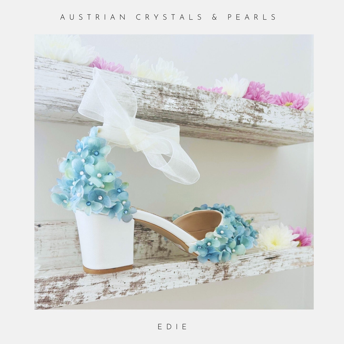 Ivory bridal shoe with floral decorations on a wooden surface, labelled 'Austrian Crystals & Pearls' and 'Edie'.
