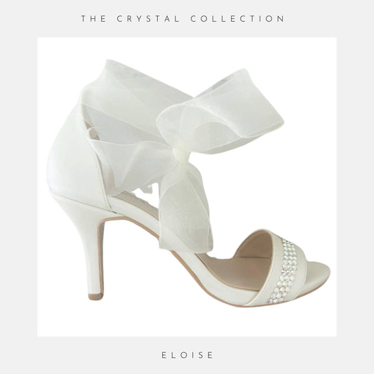 Ivory high-heeled sandal with a large bow on a light grey background, labelled 'Eloise' under 'The Crystal Collection'.