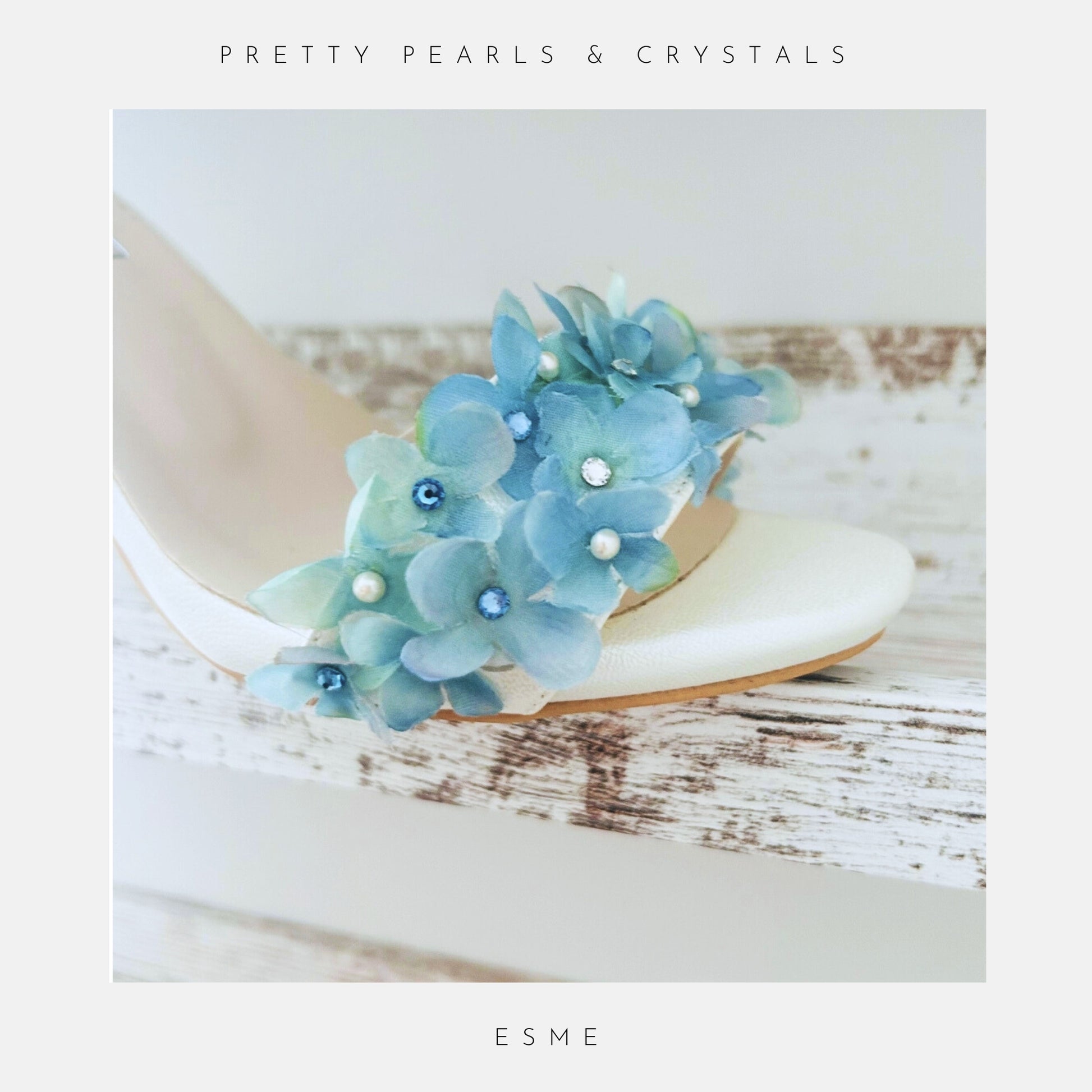 Ivory wedding sandal with blue floral embellishments on a wooden surface, labelled 'Austrian Crystals & Pearls' and 'ESME'.