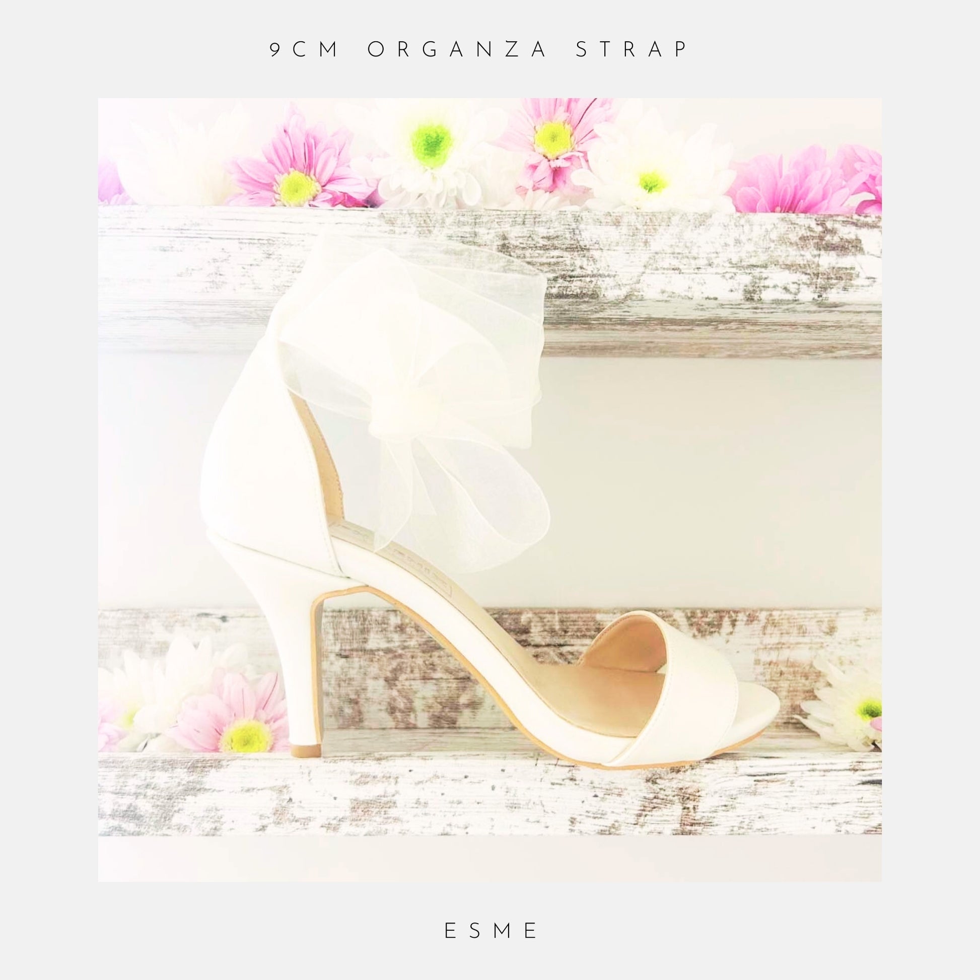 Ivory high-heeled bridal open toe shoe with a bow on a wooden surface with flowers, labelled 'The Organza Collection' and 'Esme'.