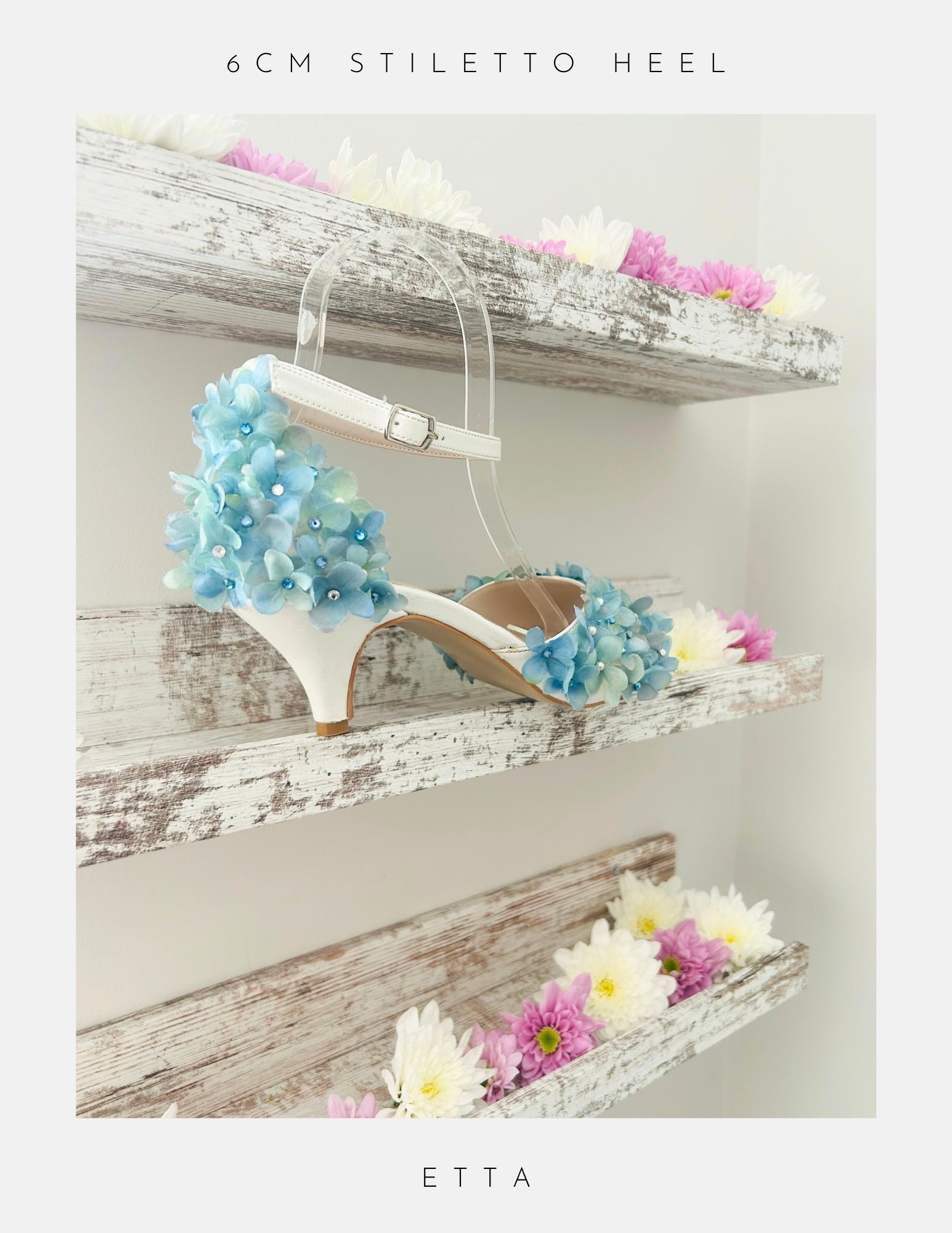 Ivory peep toe high-heeled shoe with floral design on a wooden shelf with flowers.