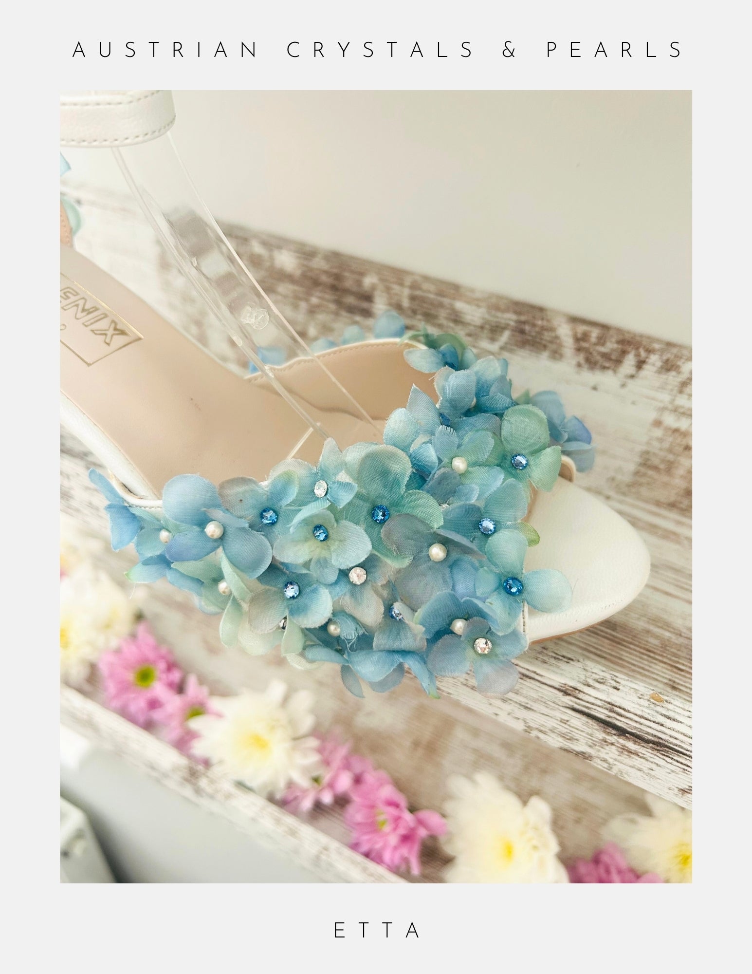Ivory bridal sandal with blue floral embellishments on a wooden surface with flowers.