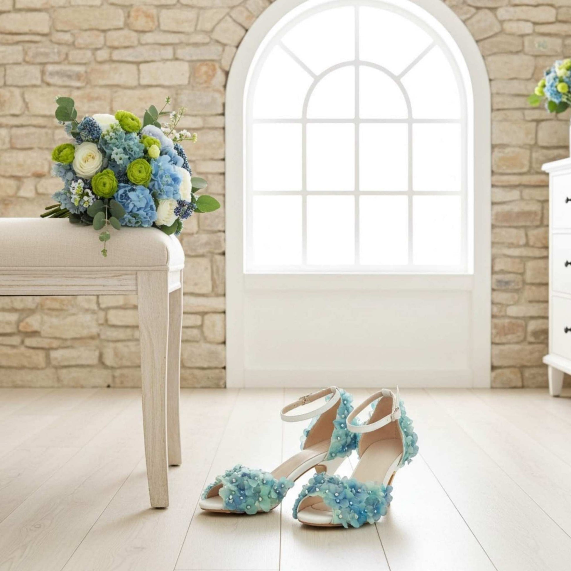 Side view of floral kitten heels on a light oak floor and bridal bouquet on a cream stool.