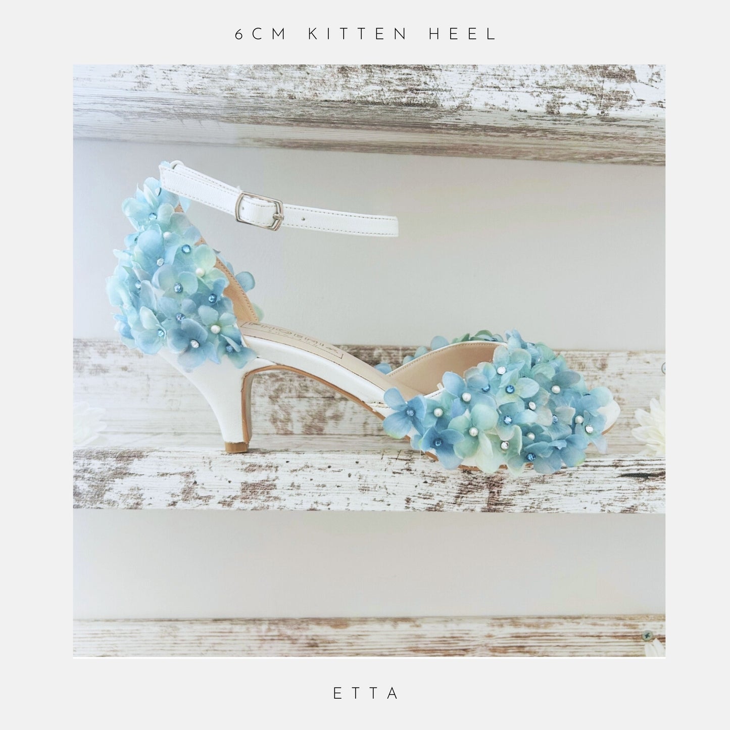 Ivory bridal shoes with blue floral decorations on a wooden surface, labelled '6CM KITTEN HEEL' and 'ETTA'.