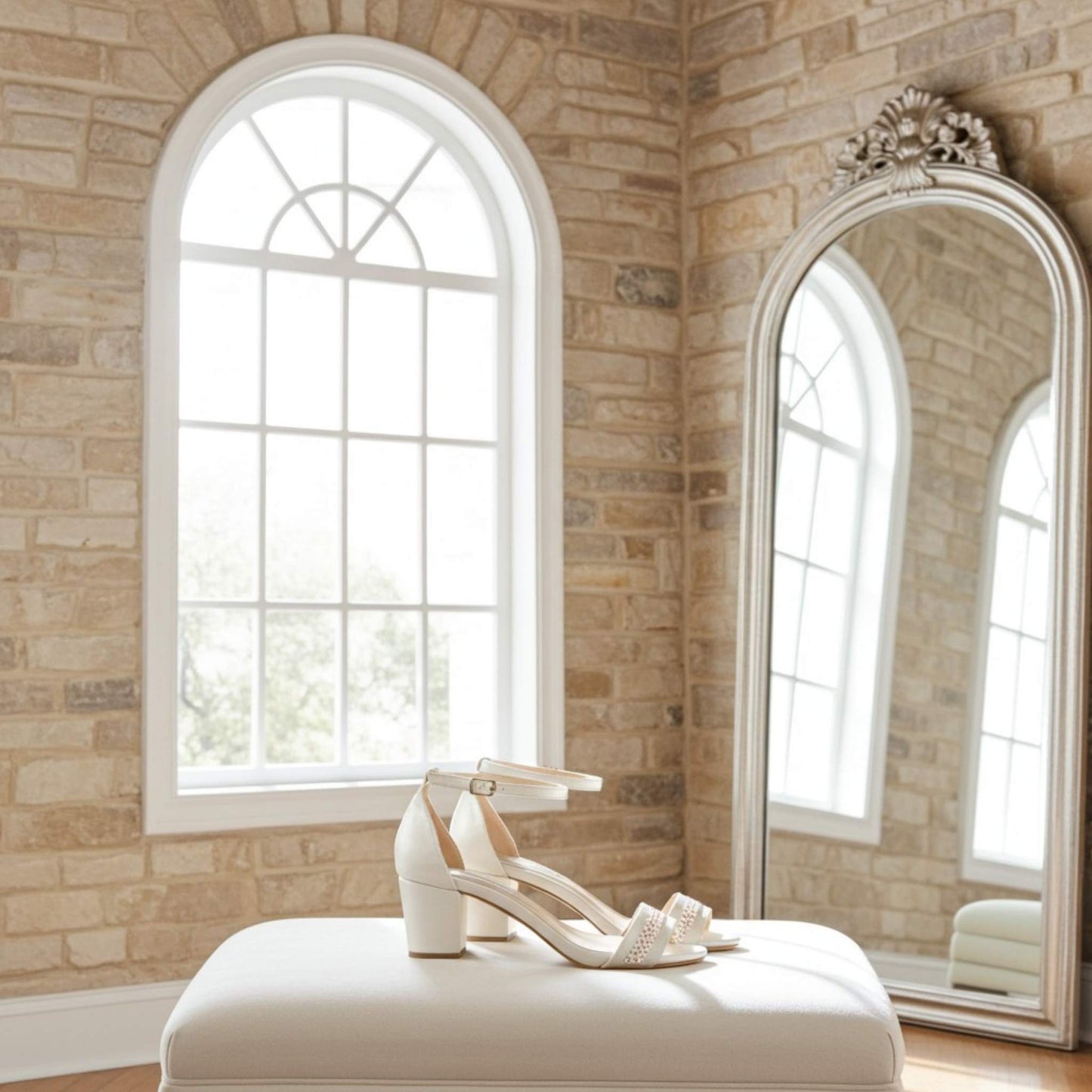 Ivory mid-heeled shoes on a white stool in front of a large mirror and window with stone walls.