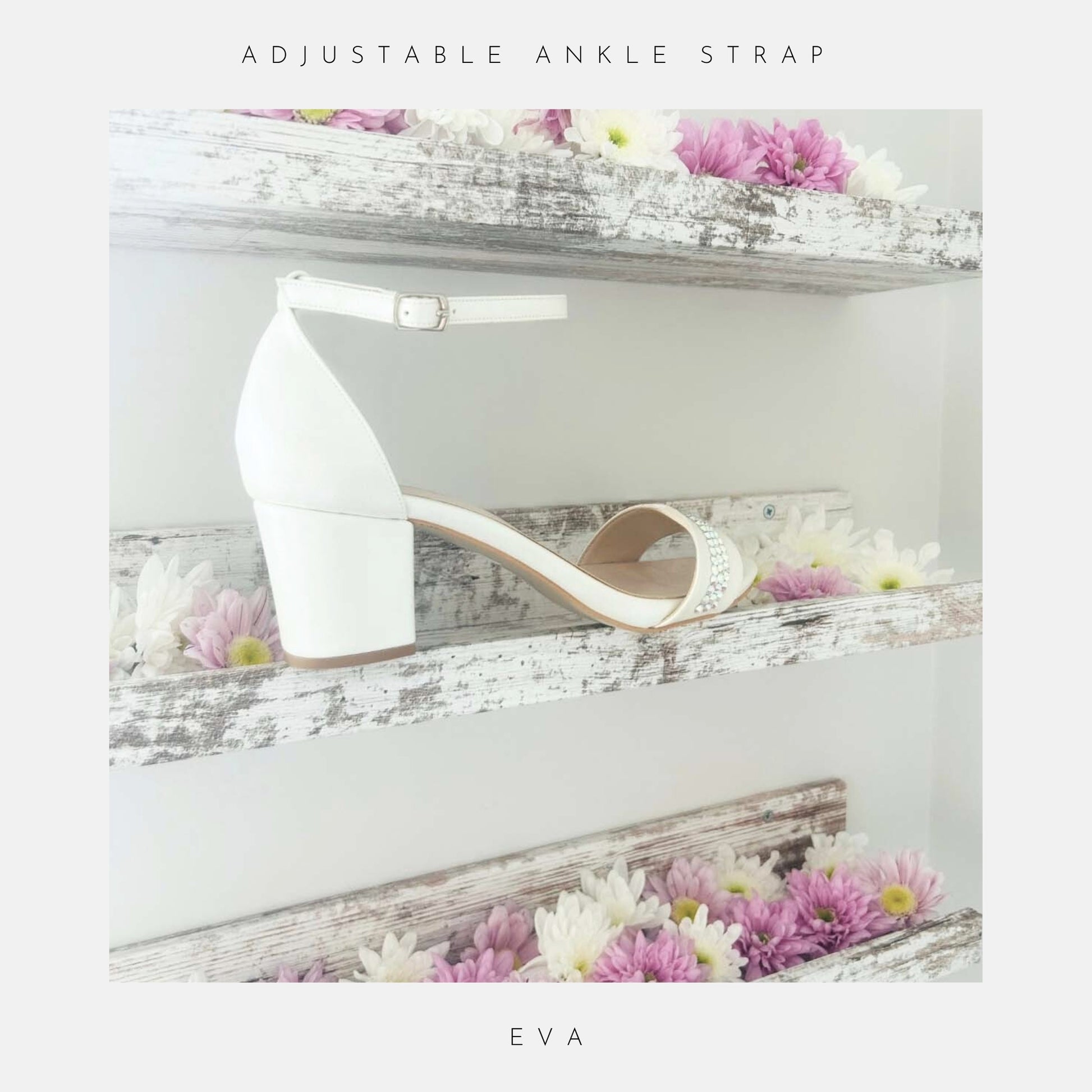 The Eva Crystal Low Block Heel Bridal Shoes by Phoenix England are ivory pearl vegan leather sandals with ankle straps and low block heels, displayed on shabby chic wooden shelves adorned with white and pink flowers.