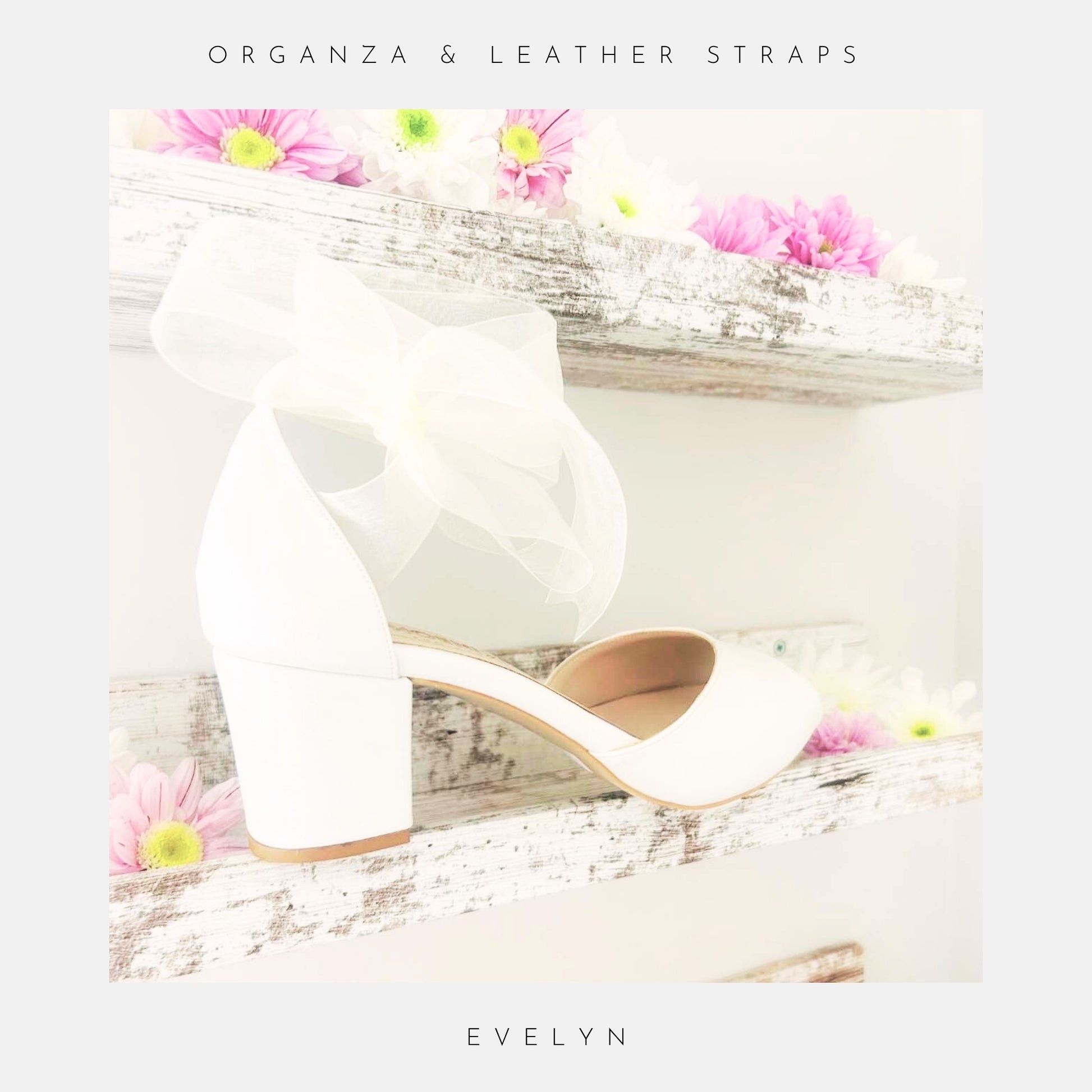 Ivory low block heel wedding shoes with a bow and straps on a wooden surface with flowers.